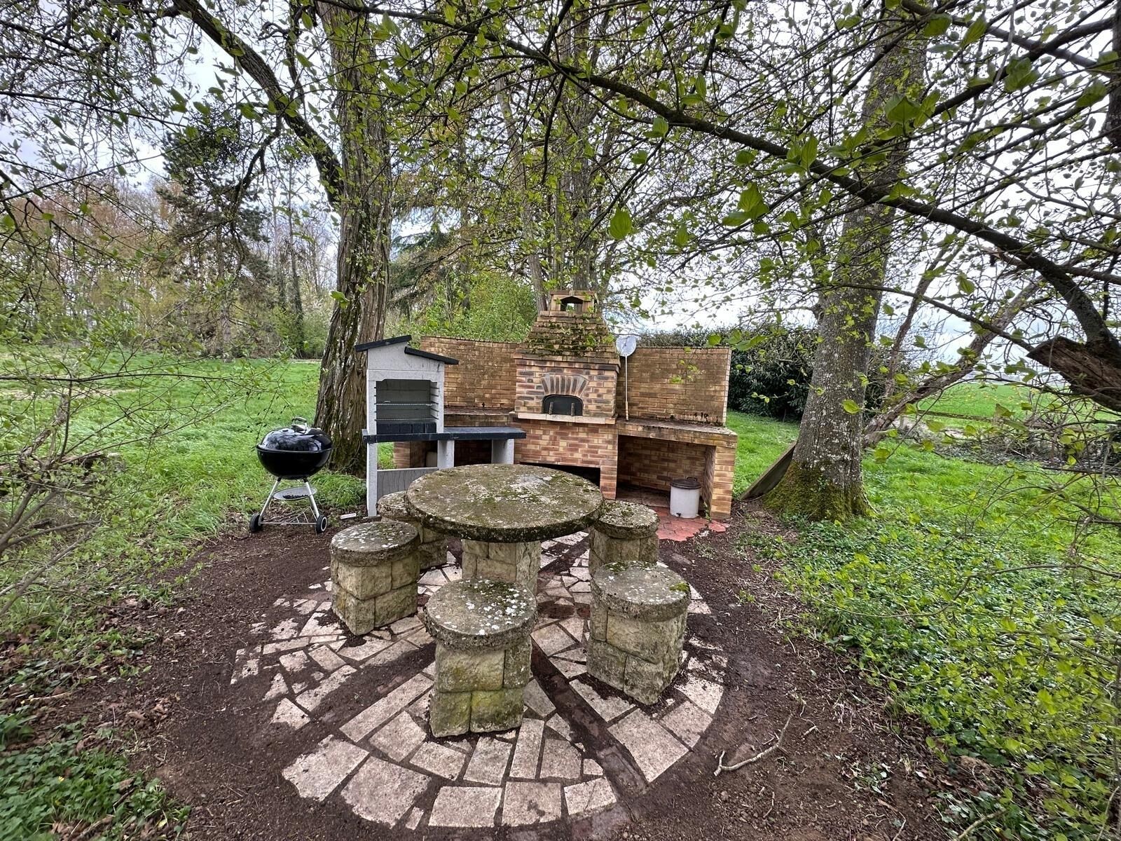 Un espace barbecue extérieur doté d’un four en briques, d’un gril et de tables en pierre.