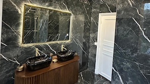 Un baño moderno con pared de mármol, tocador de madera y un espejo grande con iluminación integrada.