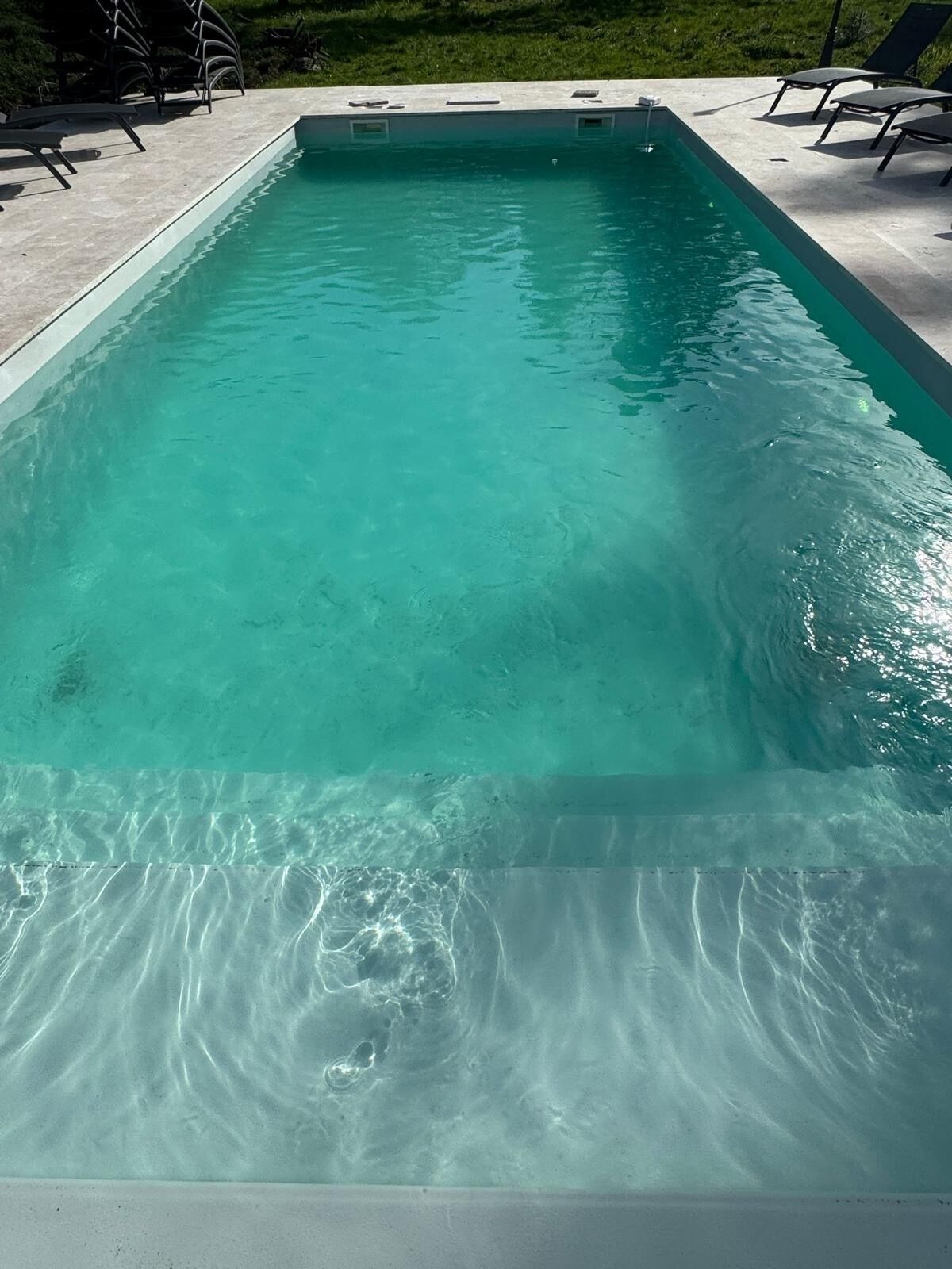 Een rechthoekig zwembad met helder water, omringd door een betonnen terras en ligstoelen.