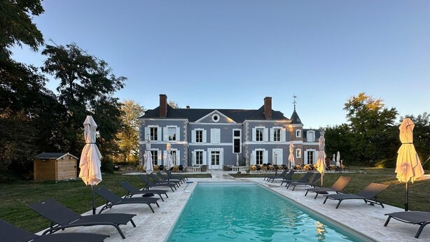 Una casa grande con piscina, rodeada de sillones de descanso y sombrillas.