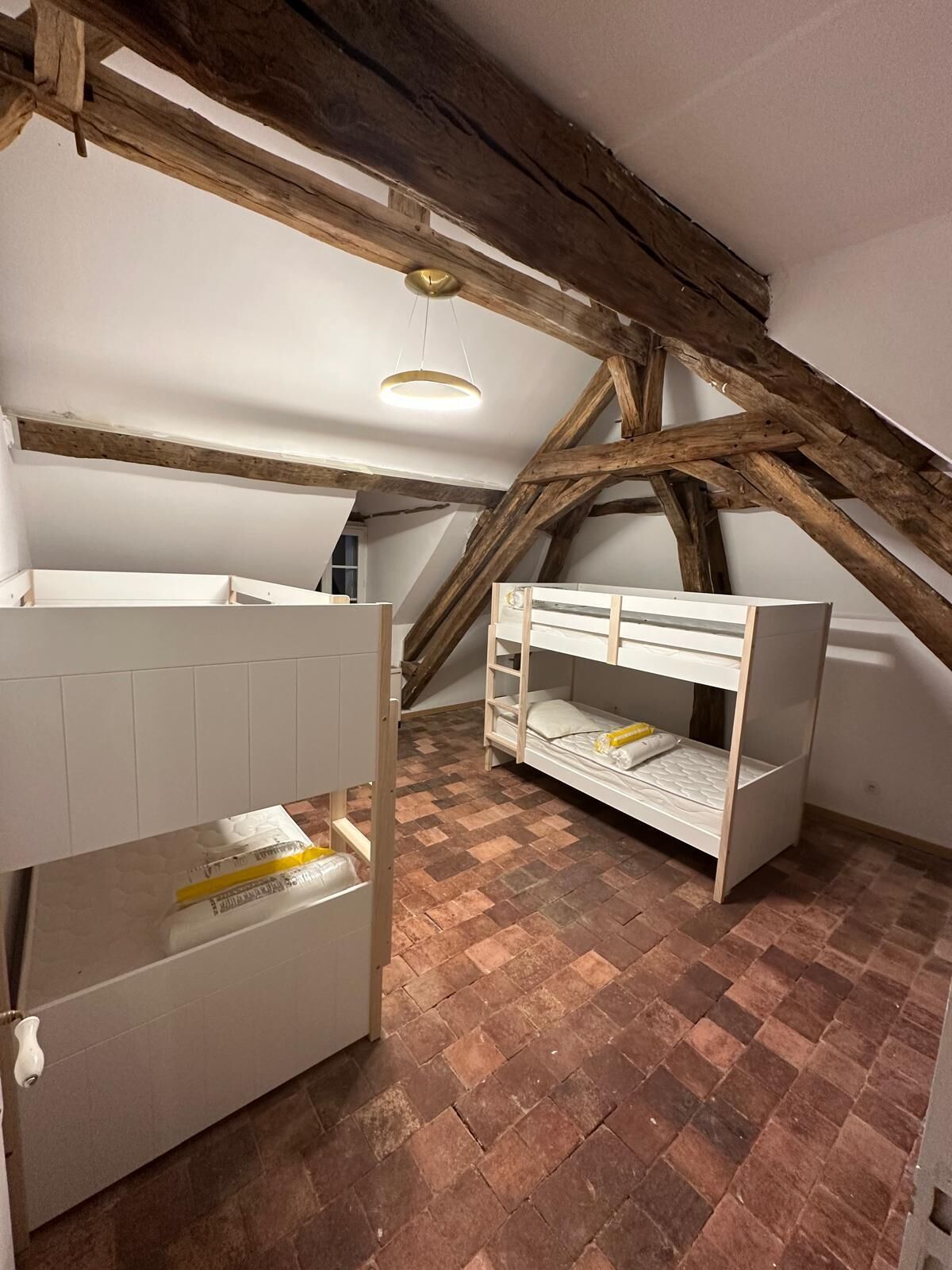 Une pièce avec des poutres apparentes, un lit en mezzanine et un mur blanc.