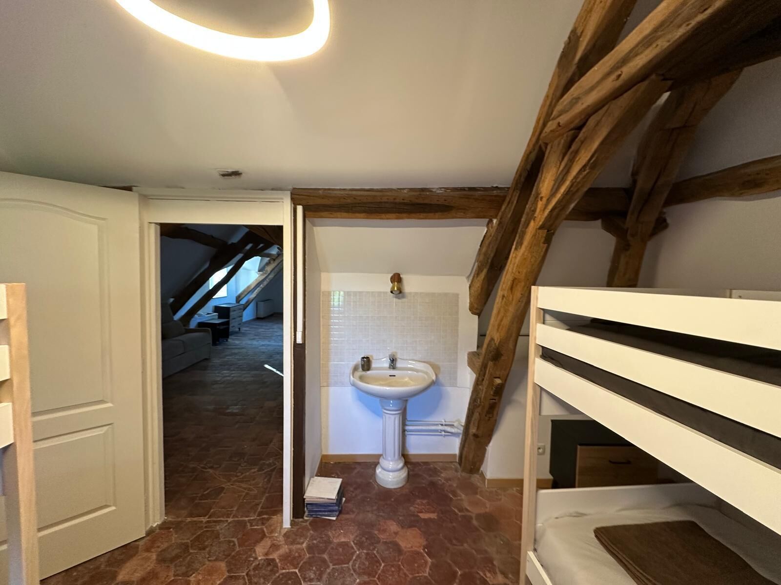 A bathroom with a white pedestal sink, a tiled wall, and a wooden ceiling beam.
