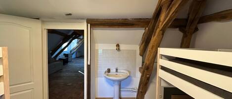 A bathroom with a white pedestal sink, a tiled wall, and a wooden ceiling beam.