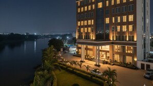 A modern hotel with a prominent sign reading "Hotel Purnima Regency." It features a multi-story structure with a well-lit entrance and a landscaped area with palm trees. - Hotel Anand Regency Riverfront (Dhule)