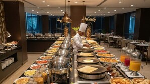A buffet setup with various food items and a chef preparing food in the background. - Hotel Anand Regency Riverfront (Dhule)