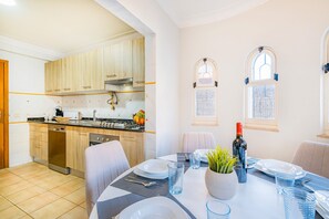 A modern kitchen with wooden cabinets, a gas stove, and a dining area with a table set for two. - Sophisticated villa with BBQ and heatable pool (Armação de Pêra)