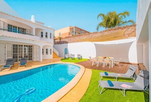 Una piscina con sillones de descanso, una mesa con sillas y un espacio cubierto de césped.