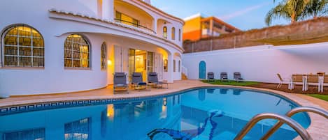 Una piscina con sillas de descanso y un edificio con ventanas de arco.