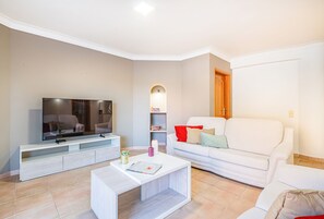 A modern living room with a flat-screen TV, a white sofa, a coffee table, and a bookshelf. - Sophisticated villa with BBQ and heatable pool (Armação de Pêra)