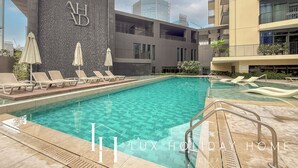 A swimming pool with lounge chairs and umbrellas, surrounded by modern buildings. - LUX The Business Bay Executive Suite (Dubai)