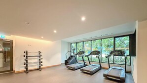 A gym with treadmills, a weight rack, and large windows with a view of greenery. - LUX The Business Bay Executive Suite (Dubai)