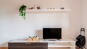A modern living room with a flat-screen TV, a white entertainment unit, a dark wood drawer, and a small plant on the wall. - Casa  Emma (isla de Fuerteventura)