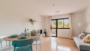 A modern living room with a dining area, large windows, and a sofa with colorful cushions. - Casa  Emma (isla de Fuerteventura)