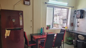 Une cuisine compacte comprenant un réfrigérateur, une table à manger avec des chaises, une fenêtre avec des barreaux et un distributeur d’eau.