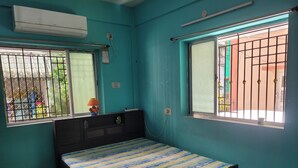 Une chambre à coucher avec un lit, deux fenêtres grillagées, un climatiseur et une petite table avec une lampe.