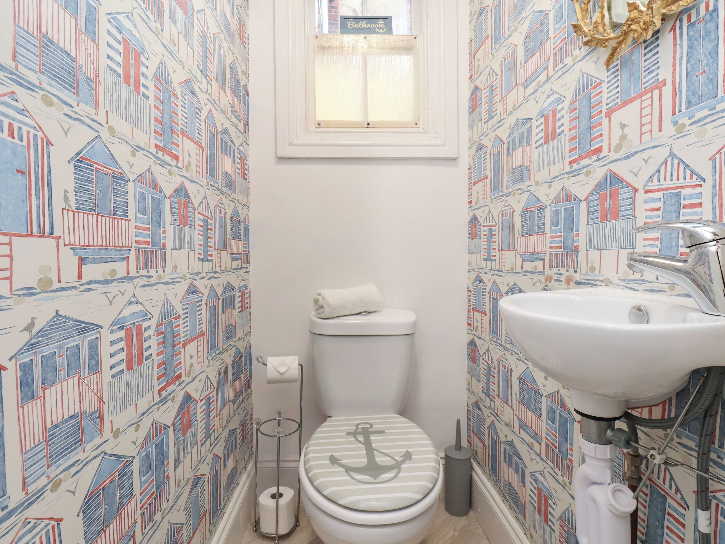 A bathroom with a nautical-themed wallpaper, a toilet, a sink, and a window above the toilet.