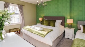 Een verzorgde slaapkamer met een groot bed, twee nachtkastjes, een kroonluchter en een raam met gordijnen.