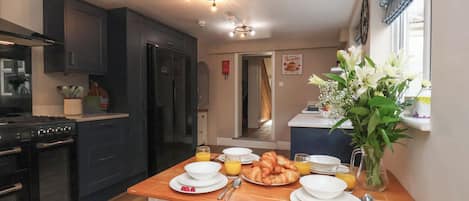 A modern kitchen with dark cabinets, a stove, and a dining area with a wooden table set for breakfast.