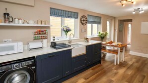 Een moderne keuken met een ingebouwde wasmachine, een groot raam met gestreepte gordijnen, en een eethoek met een houten tafel en stoelen.