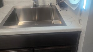 Eine Küche mit Spüle aus Edelstahl, dunklen Holzschränken und einer weißen Arbeitsplatte.