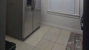 Eine Küche mit einem Edelstahlkühlschrank, einem Fenster mit Jalousien und einem gefliesten Boden.