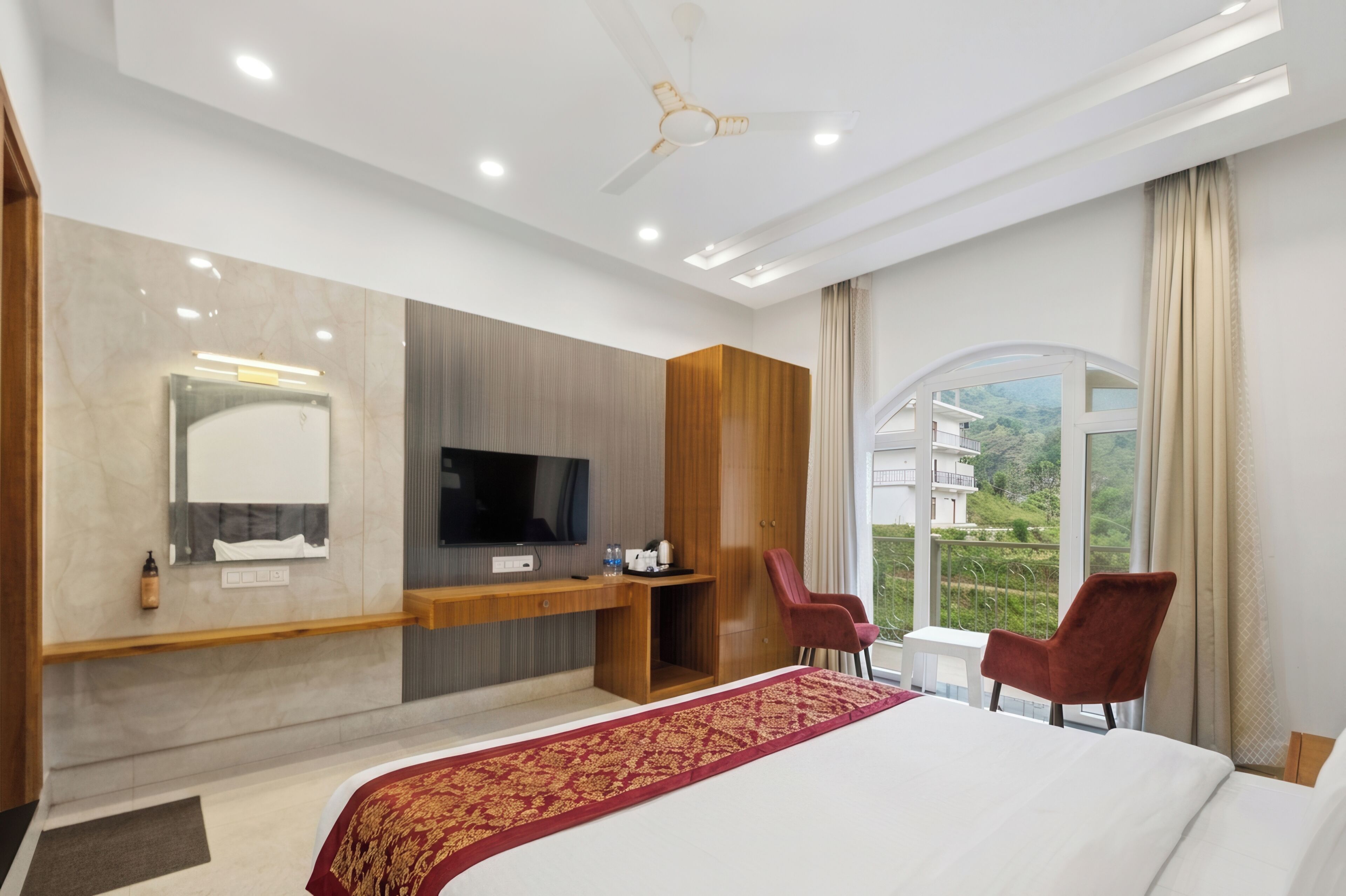 A hotel room with a bed, a TV, a desk, a chair, and a view of greenery.