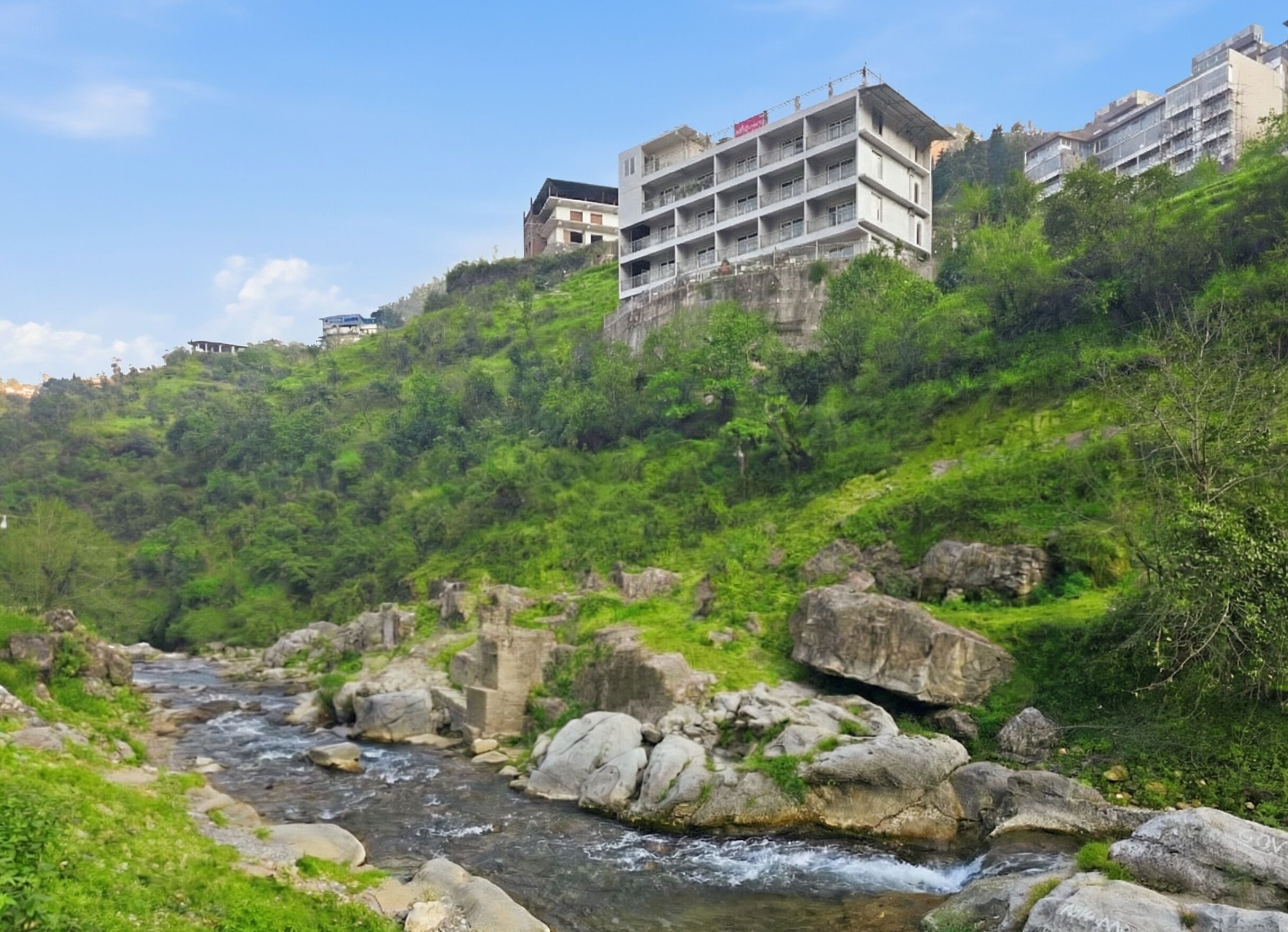 A river flowing through a rocky landscape with lush greenery and buildings in the background.