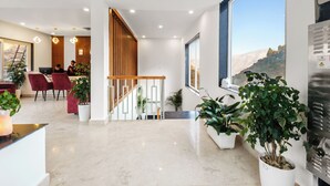 A modern hotel lobby with a marble floor, wooden staircase, and large windows offering a mountain view. - Palm Aryan Pause by the Stream Resort (Dhanaulti)