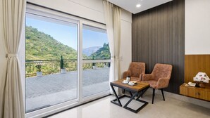 A modern hotel room with a balcony, two plush armchairs, a small wooden table, and a nightstand with a lamp. - Palm Aryan Pause by the Stream Resort (Dhanaulti)