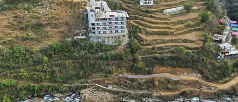 A multi-story building with a green roof, situated on a terraced hillside with a winding road.