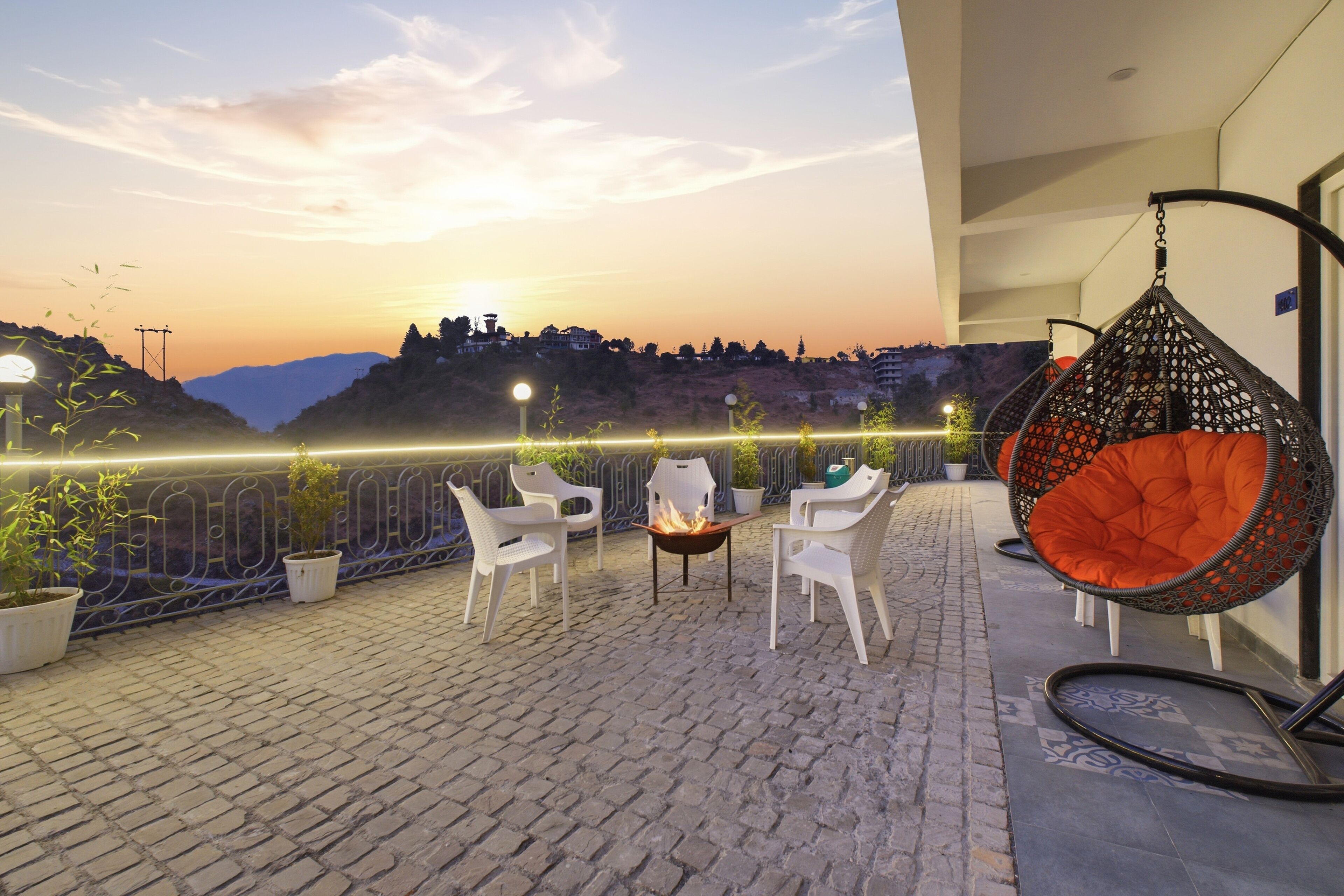 Une terrasse sur le toit avec des chaises blanches, un fauteuil suspendu et un foyer.