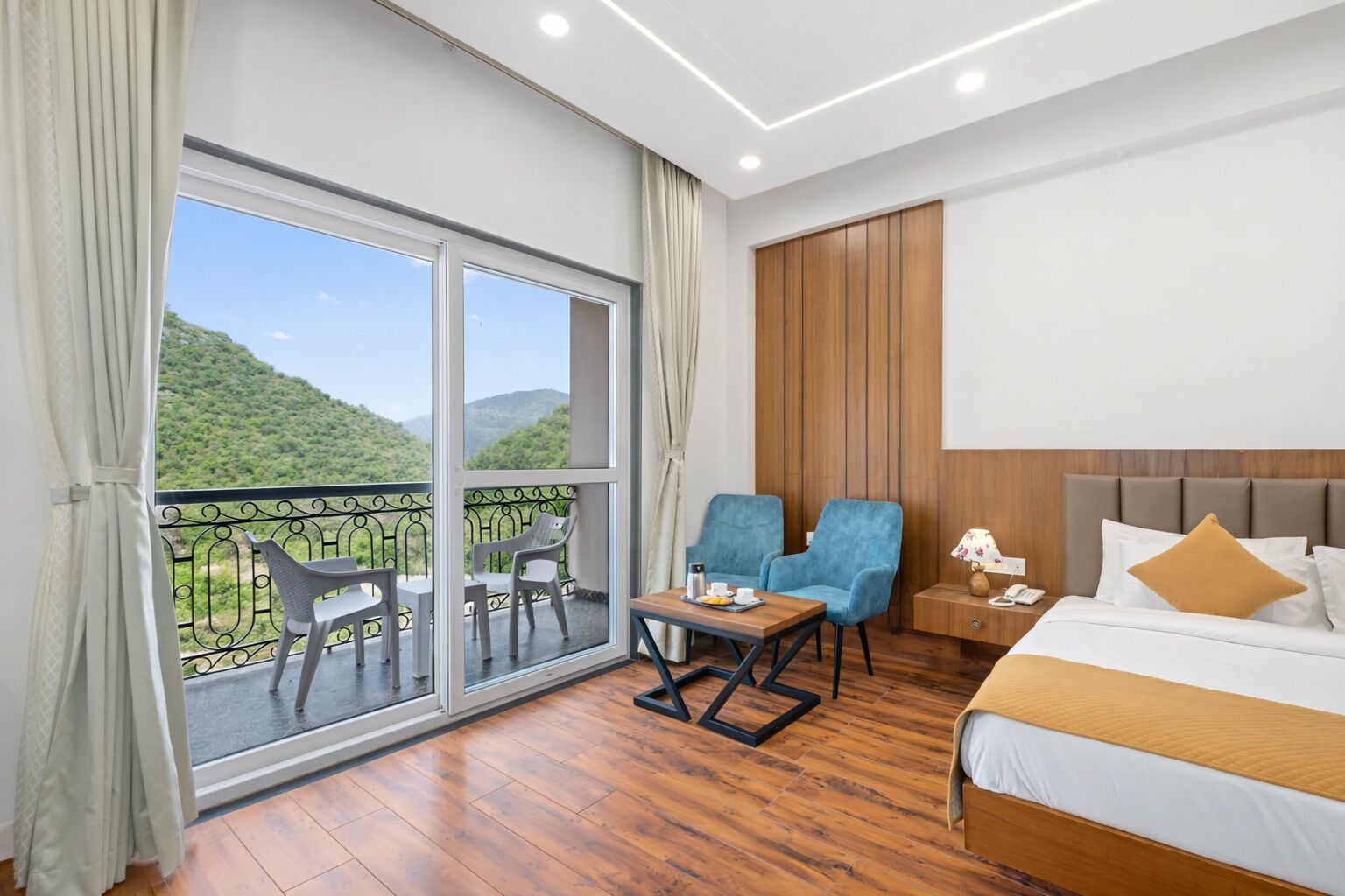 A hotel room with a balcony, a bed, two chairs, a table, and a nightstand.