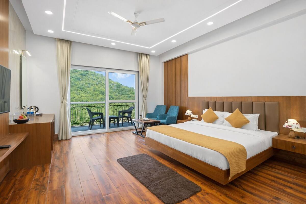 Una habitación de hotel moderna con una cama grande, un escritorio con una silla, un balcón con sillas y un televisor.