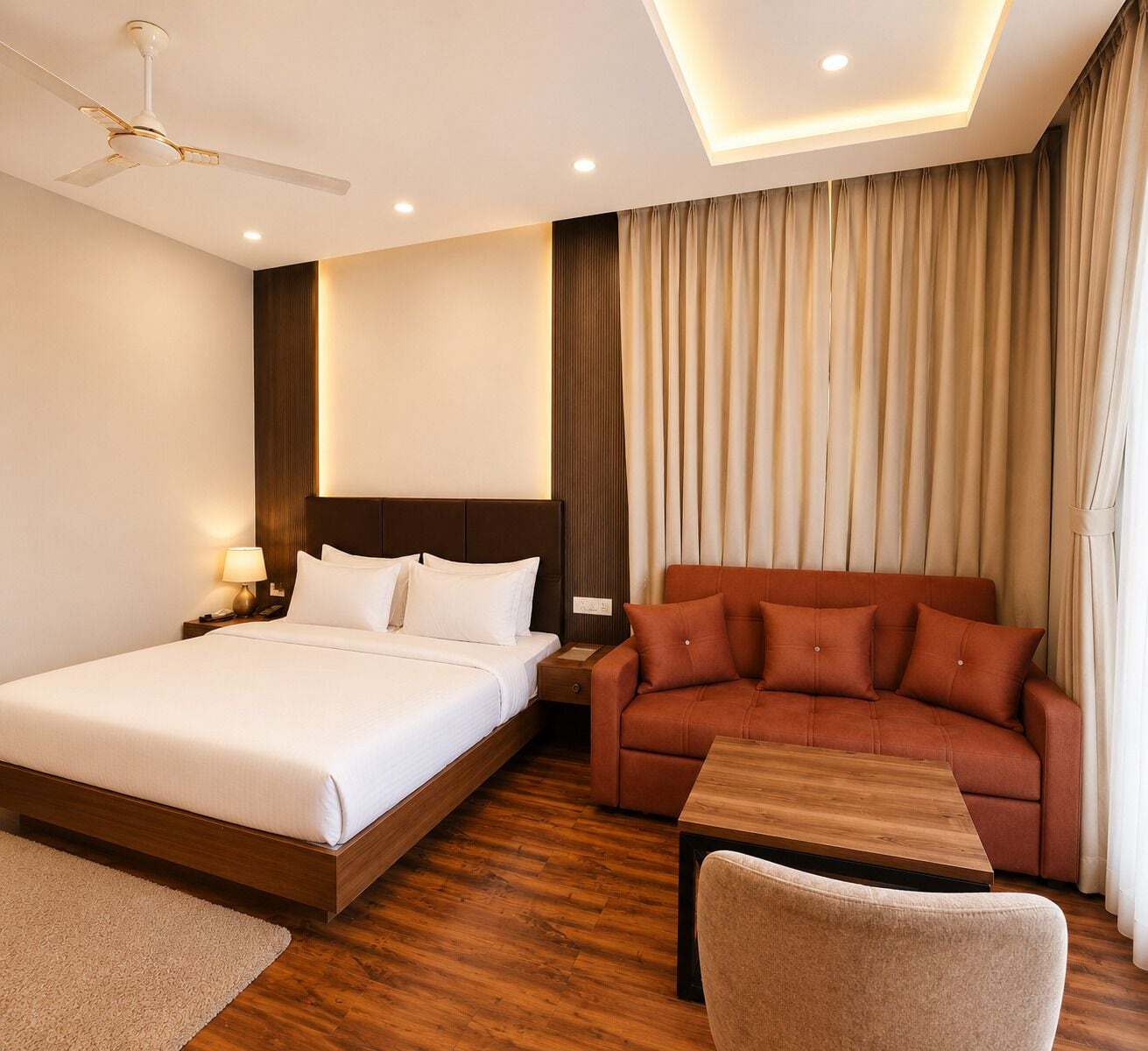 A hotel room with a bed, a sofa, a desk, a chair, a ceiling fan, and curtains.