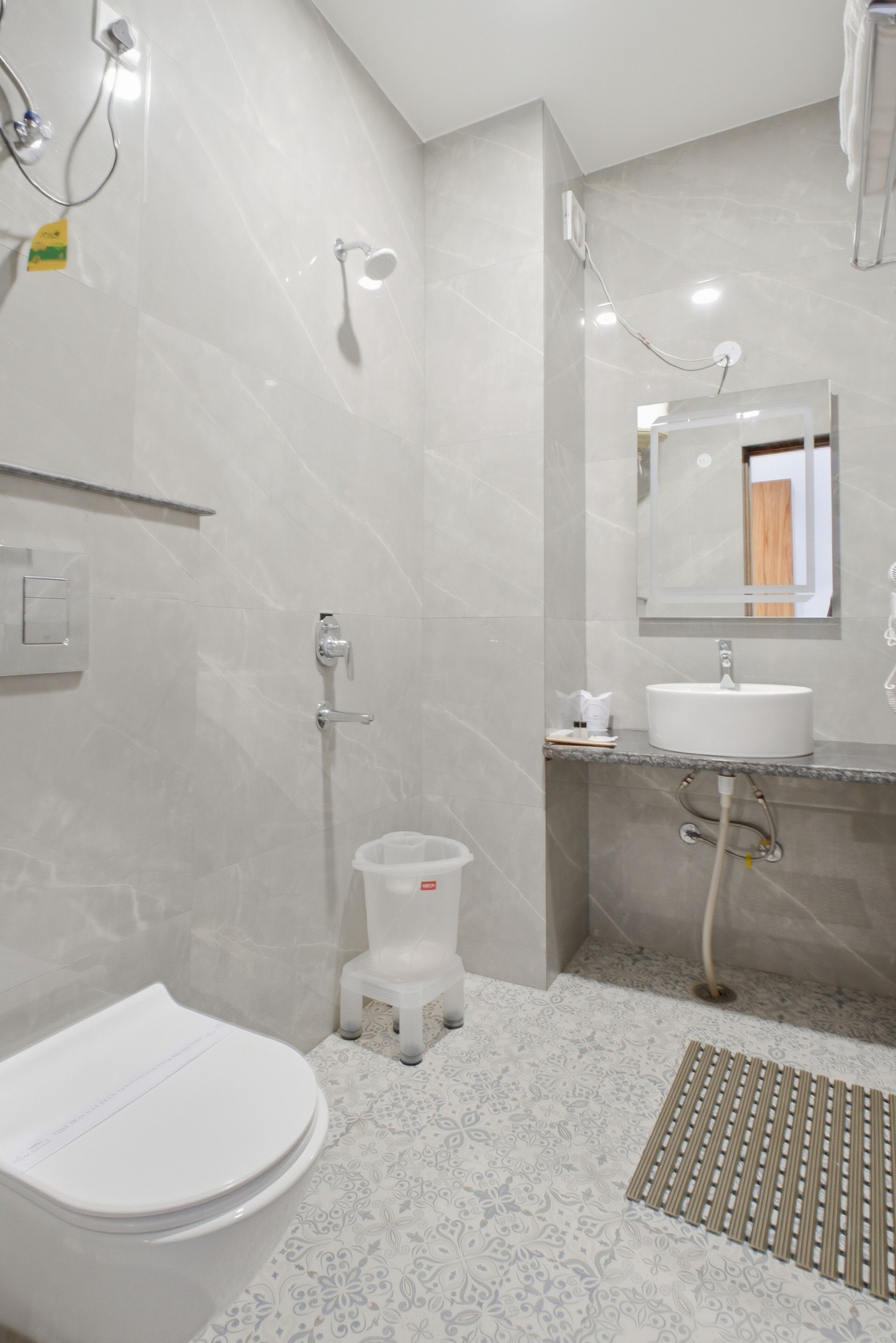 Uma casa de banho moderna com sanita, lavatório, chuveiro e um pequeno contentor de lixo.