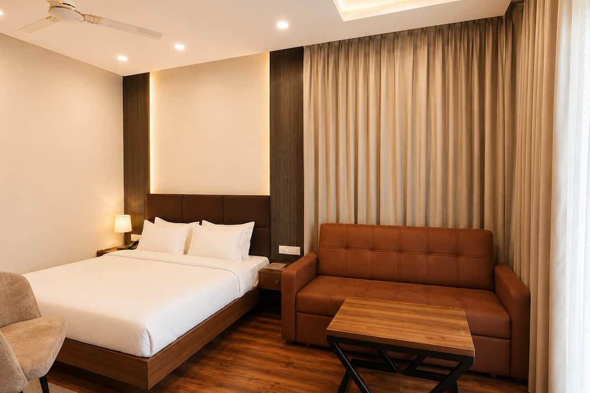 Habitación de hotel con cama, sofá, una mesita, una silla, ventilador de techo y ventana con cortinas.