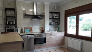 Une cuisine avec des meubles blancs, une cuisinière, un lave-vaisselle et une fenêtre donnant sur un paysage verdoyant.