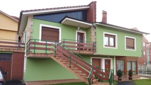 Une maison à deux étages avec une façade verte, un escalier en bois et un petit porche à l’avant.