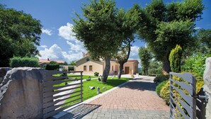 Un vialetto lastricato conduce a un edificio con tetto in tegole rosse, circondato da vegetazione e un muro in pietra.