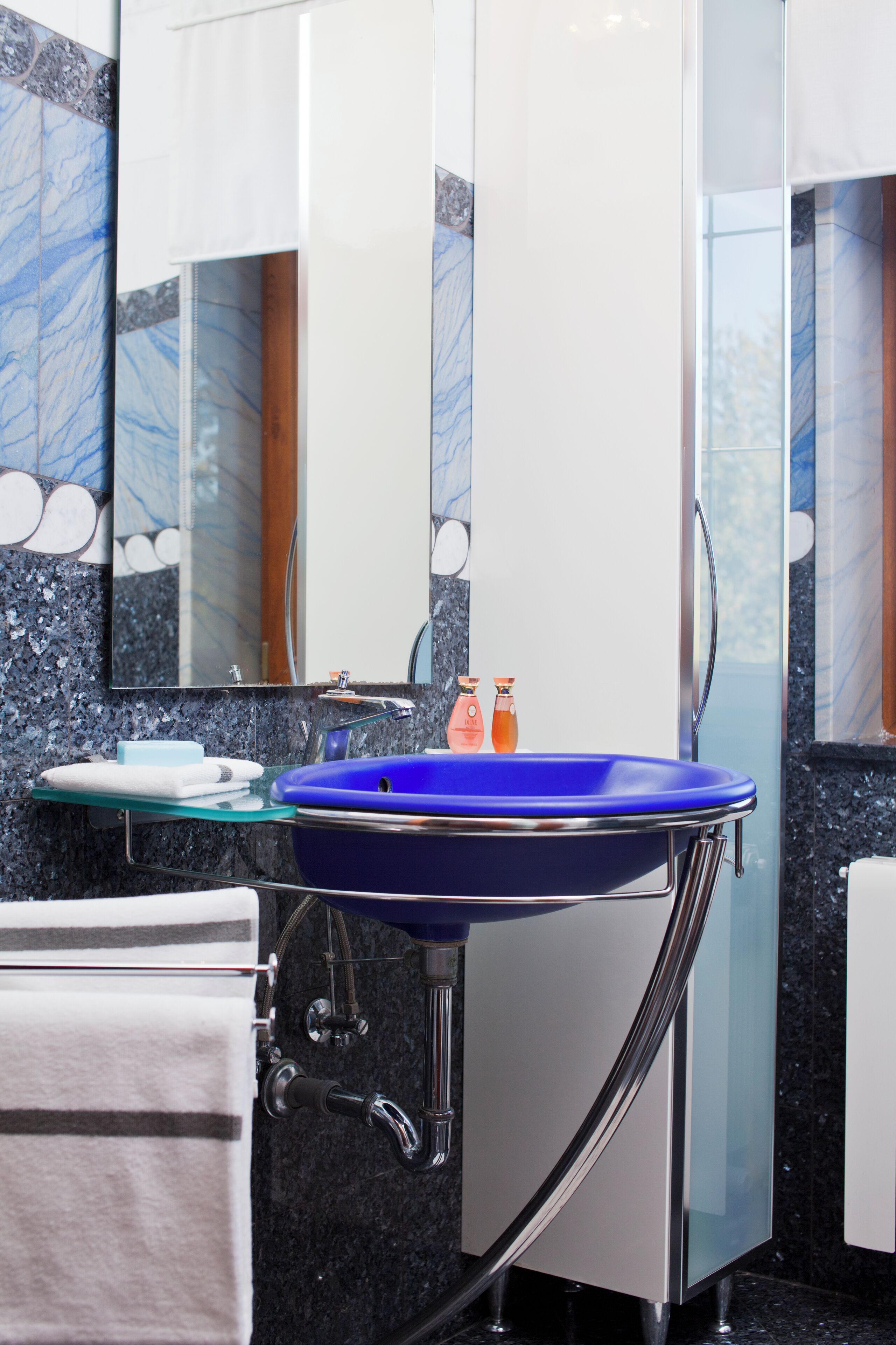 Ein modernes Badezimmer mit einem blauen Waschbecken, einer Glasablage und einem großen Spiegel.