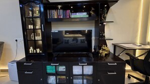 A modern entertainment unit with a flat-screen TV, shelves with books and decorative items, and a desk with a chair. - Room With AirPurifier ,Recliner Near kolkata Airprot, CC2 and Convention Center (Kolkata)
