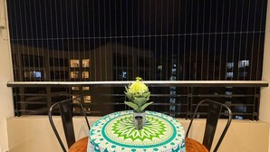 A balcony with a round table covered in a patterned tablecloth, two wooden chairs, and a potted plant with yellow flowers. - Room With AirPurifier ,Recliner Near kolkata Airprot, CC2 and Convention Center (Kolkata)