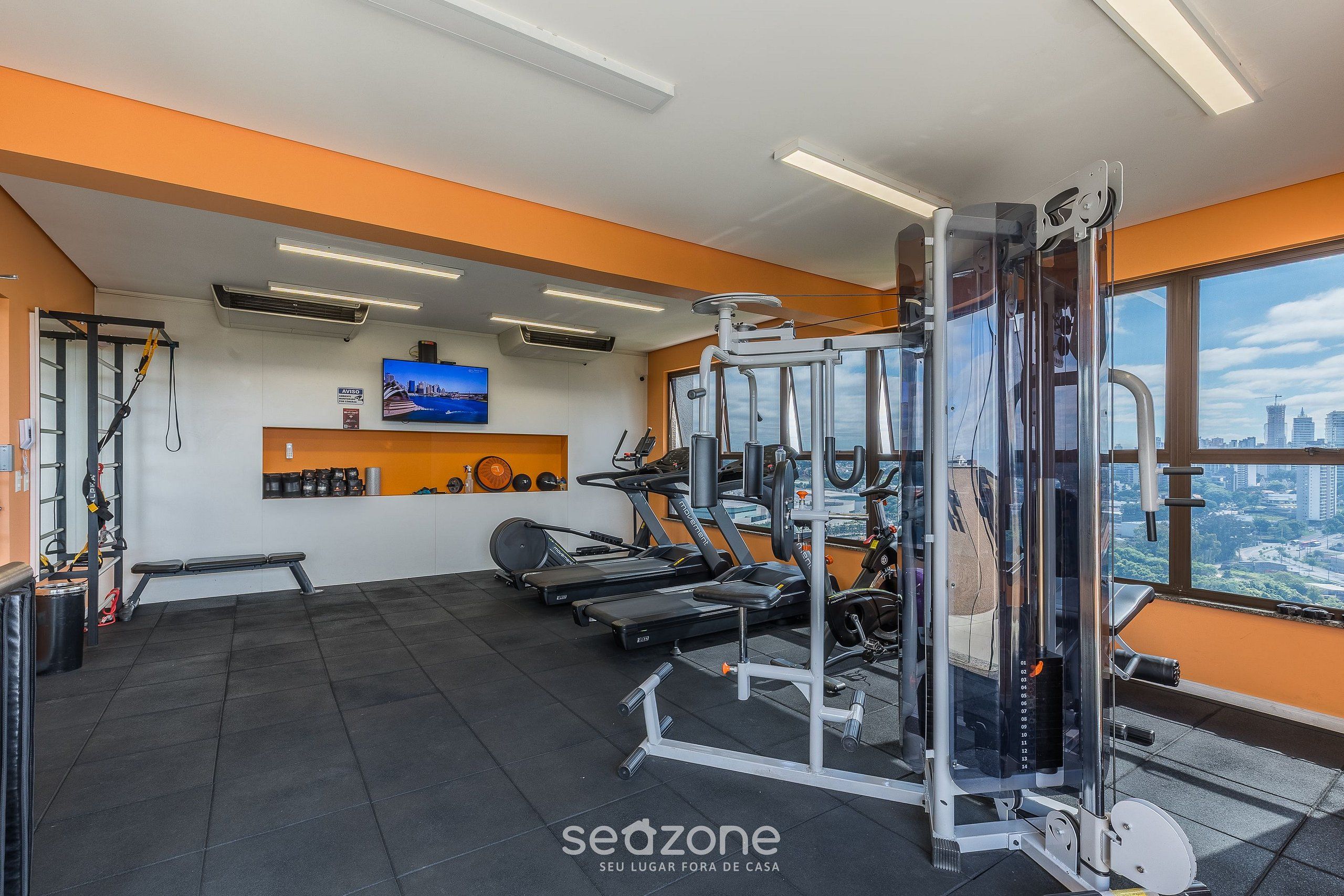 A gym with exercise equipment, a bench, and a TV on the wall.