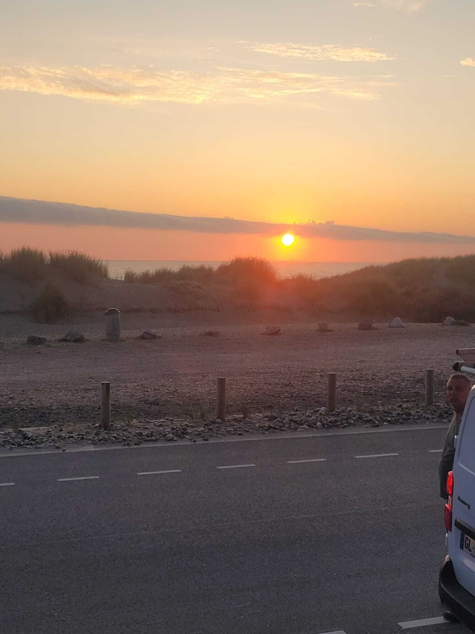 A sunset over a beach with a road in the foreground.
