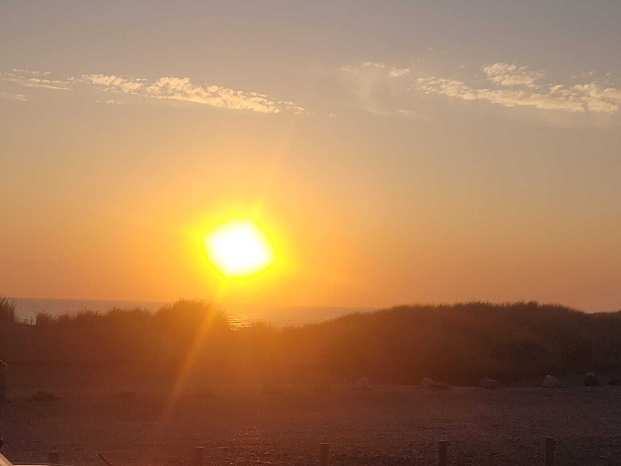 Een zonsondergang boven een strand, met een hek op de voorgrond.