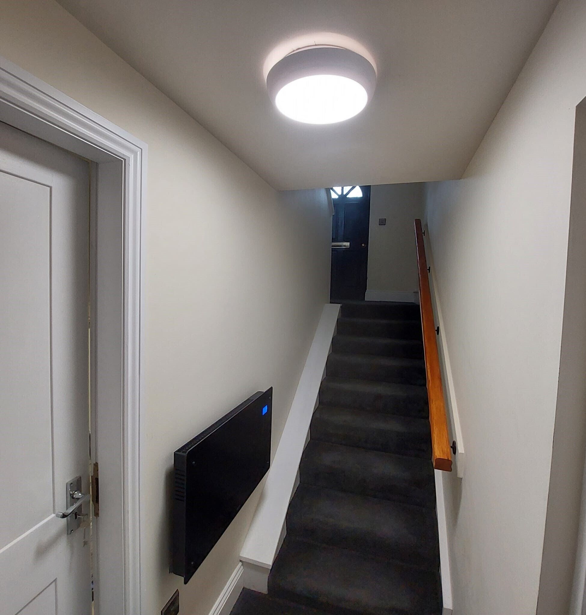 Ein schmaler Korridor mit Teppichstufen, einem an der Wand befestigten Flachbildfernseher und einer Tür am Ende.