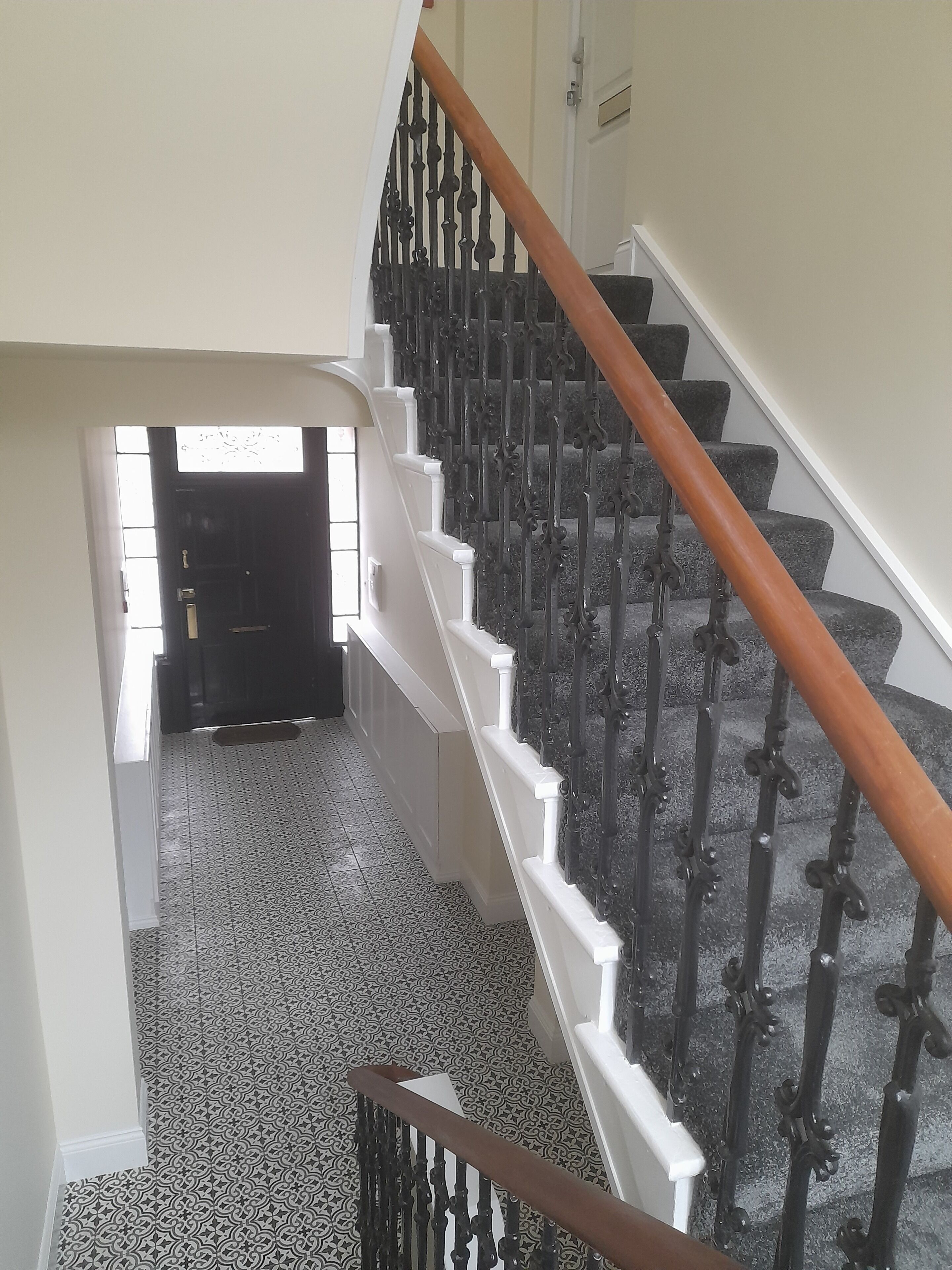 A staircase with a white handrail and black balusters, leading to a door with a window.