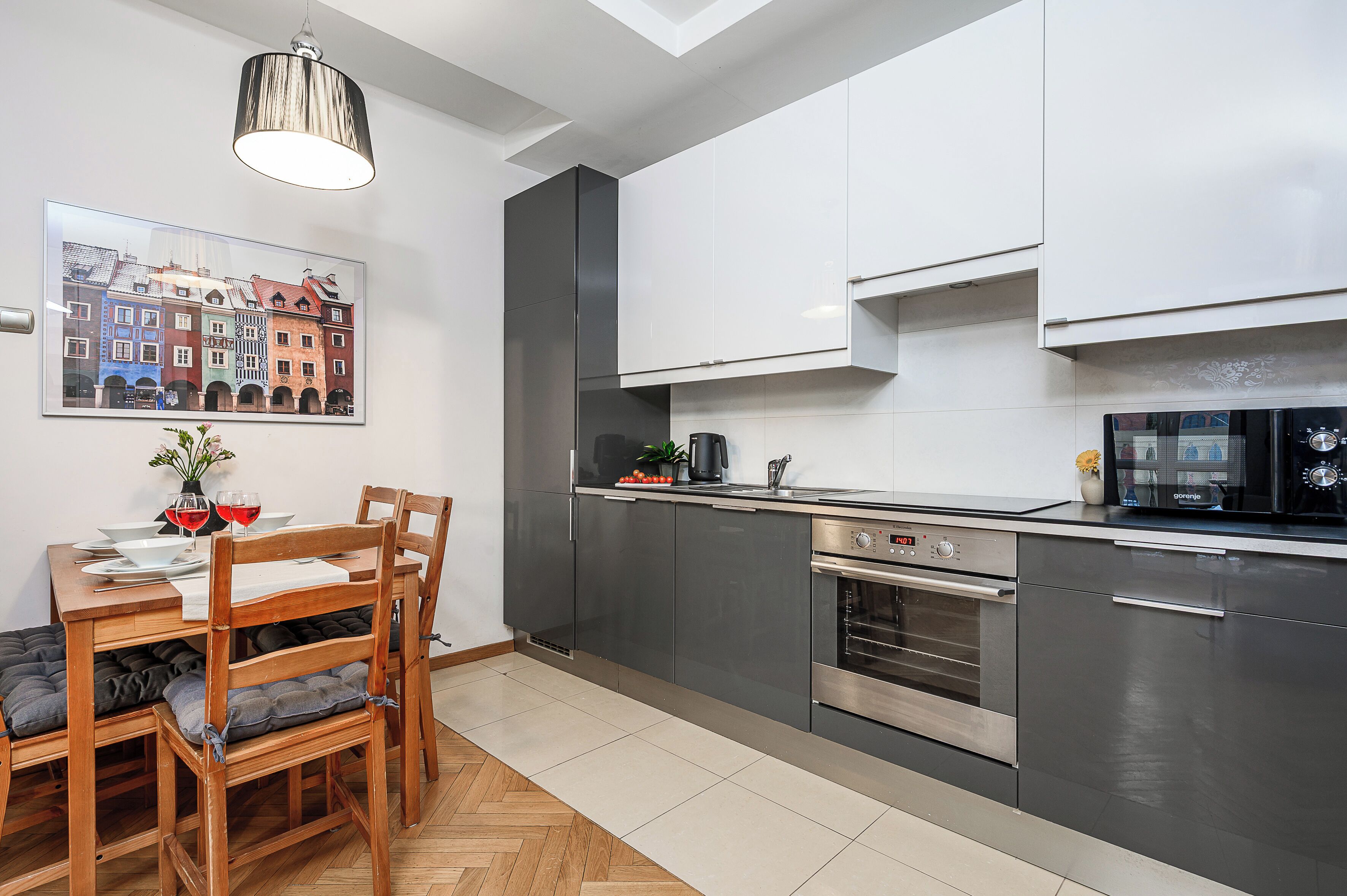 Una cocina moderna con armarios grises, un horno de acero inoxidable y una zona de comedor con sillas y mesa de madera.