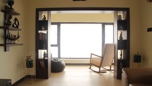 Una sala de estar con un ventanal grande, una mecedora, un sillón de felpa y estantes con adornos.