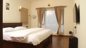 Habitación de hotel con cama, cortinas, ventilador, televisión y una pequeña mesa con una planta.